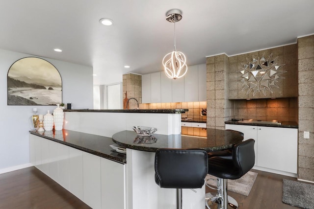 kitchen featuring white cabinetry, tasteful backsplash, decorative light fixtures, dark stone countertops, and dark hardwood / wood-style floors