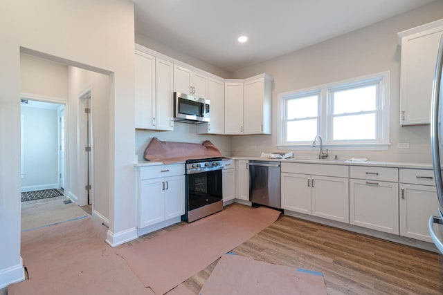 kitchen with sink, light hardwood / wood-style flooring, white cabinets, and appliances with stainless steel finishes