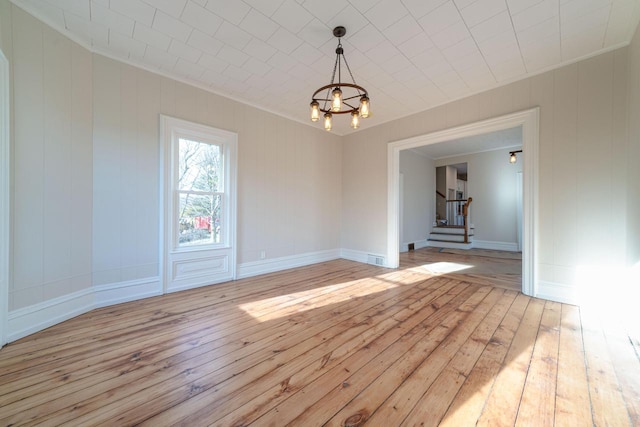 empty room with ornamental molding, a chandelier, and light hardwood / wood-style flooring