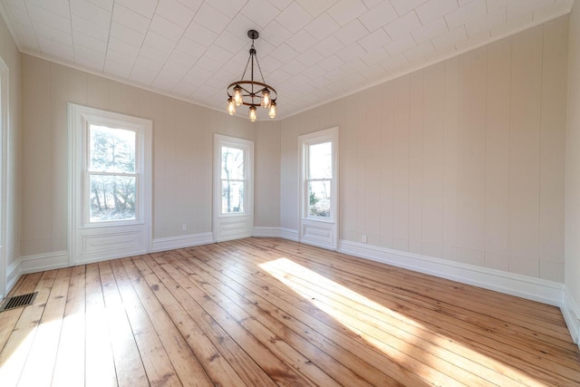 empty room with ornamental molding, a notable chandelier, and light hardwood / wood-style flooring