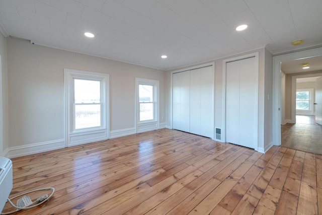 unfurnished bedroom with light hardwood / wood-style flooring and multiple closets