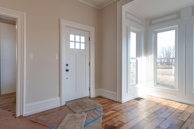 foyer with ornamental molding, a wealth of natural light, and light hardwood / wood-style floors