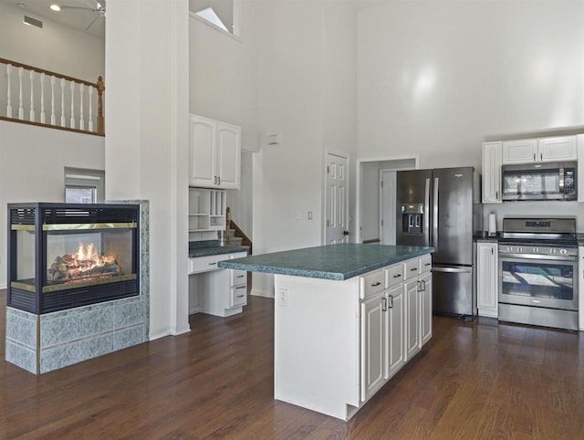 kitchen with a multi sided fireplace, a kitchen island, appliances with stainless steel finishes, dark hardwood / wood-style floors, and white cabinets