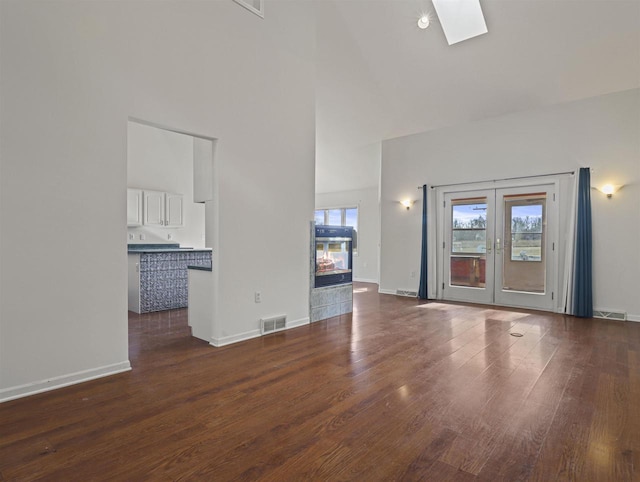 unfurnished living room featuring a high ceiling, a skylight, dark wood-type flooring, and french doors