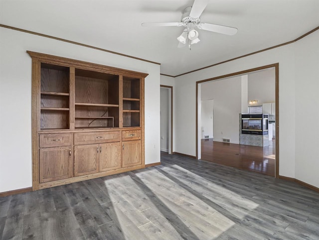 unfurnished living room featuring wood-type flooring, ornamental molding, ceiling fan, and a multi sided fireplace