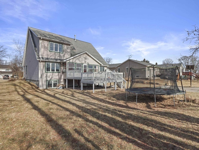 back of property with a wooden deck, a trampoline, and a lawn