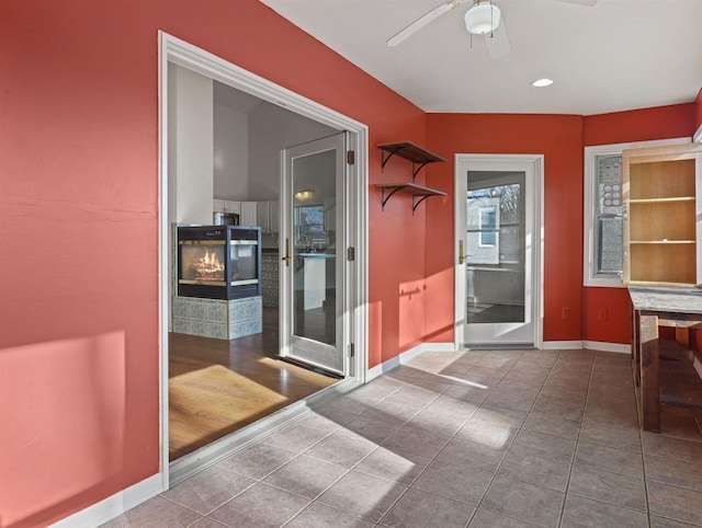 entryway with tile patterned flooring, a multi sided fireplace, and ceiling fan