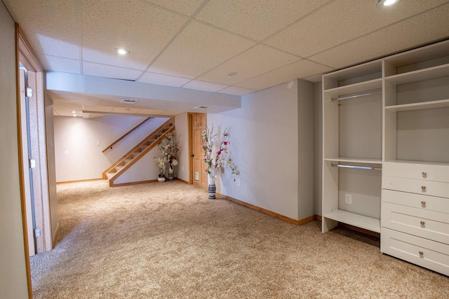 basement with a paneled ceiling and light colored carpet