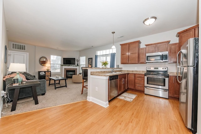 kitchen featuring decorative light fixtures, a brick fireplace, light wood-type flooring, kitchen peninsula, and stainless steel appliances