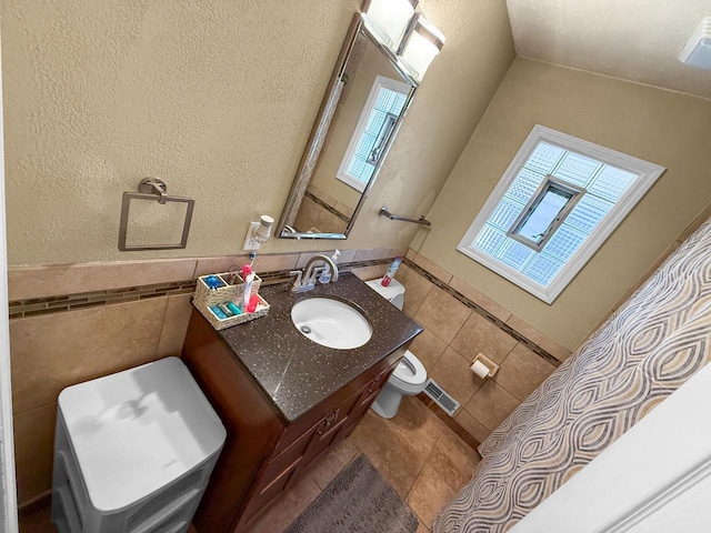 bathroom with lofted ceiling, tile walls, tile patterned flooring, vanity, and toilet