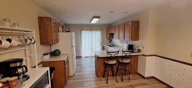 kitchen with a kitchen breakfast bar, light hardwood / wood-style floors, decorative backsplash, kitchen peninsula, and white fridge