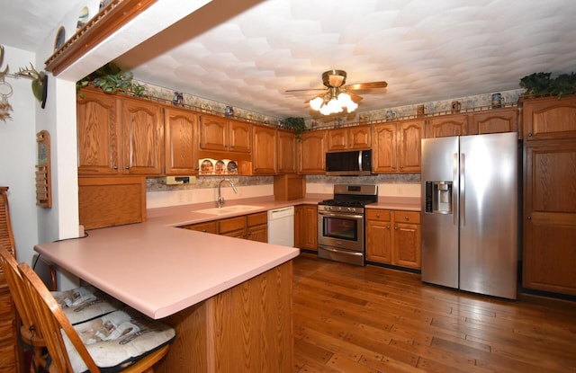 kitchen with sink, dark hardwood / wood-style flooring, kitchen peninsula, ceiling fan, and stainless steel appliances