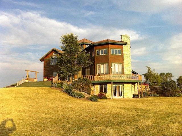 rear view of house with a deck, stone siding, a lawn, and a chimney