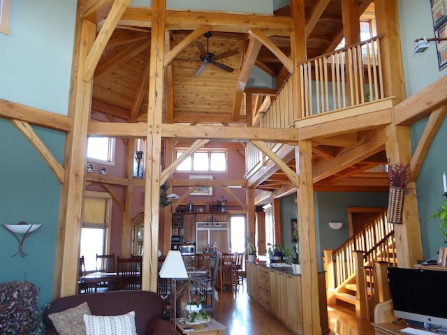 living room featuring ceiling fan, high vaulted ceiling, wood finished floors, stairs, and beamed ceiling