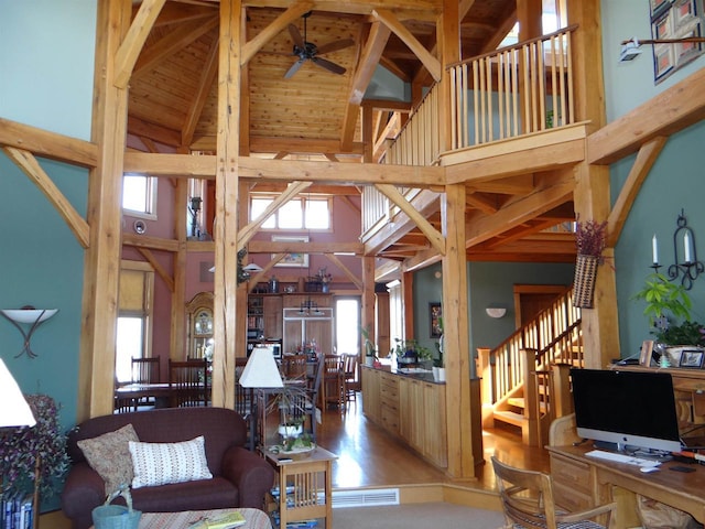 living area featuring a ceiling fan, light wood-style floors, high vaulted ceiling, beamed ceiling, and stairs