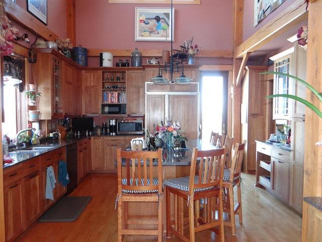 kitchen featuring glass insert cabinets, light wood-type flooring, black appliances, pendant lighting, and a sink