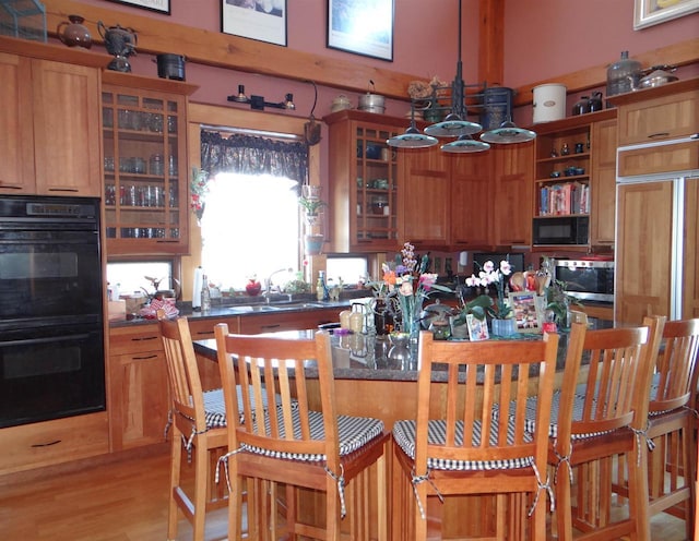 kitchen with dobule oven black, dark countertops, glass insert cabinets, stainless steel microwave, and a sink