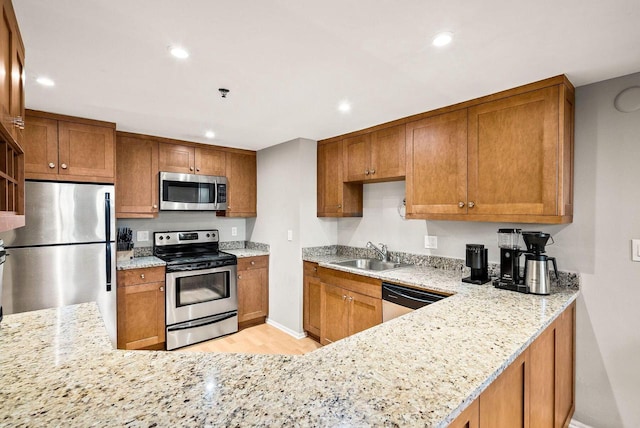 kitchen featuring appliances with stainless steel finishes, sink, kitchen peninsula, light stone countertops, and light wood-type flooring