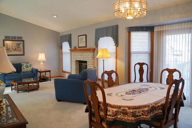 dining room featuring vaulted ceiling, a chandelier, light colored carpet, and a fireplace