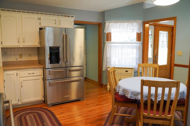 kitchen with high end fridge, backsplash, white cabinetry, and light wood-type flooring