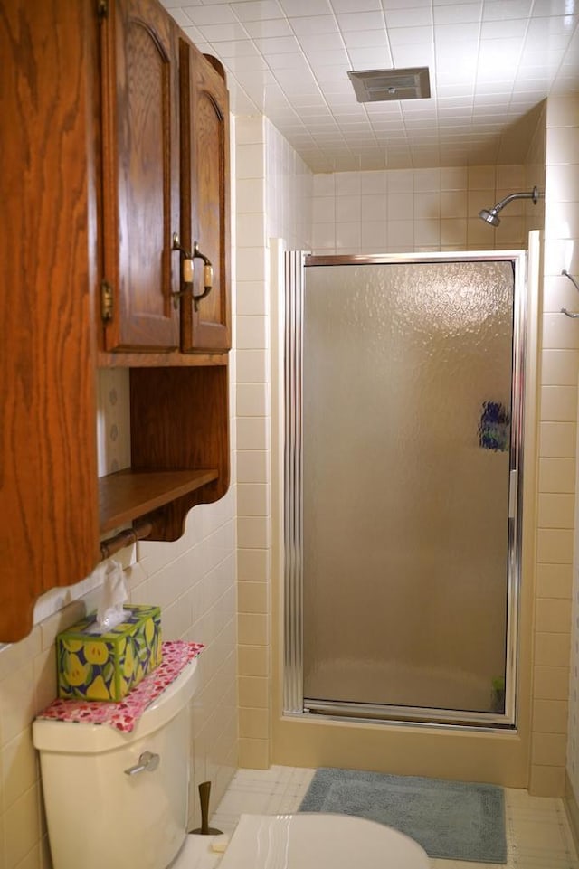 bathroom featuring a shower with shower door, tile walls, and toilet