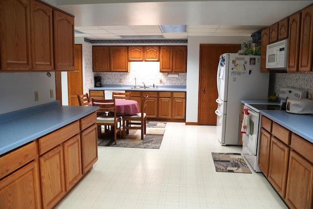 kitchen featuring tasteful backsplash, white appliances, sink, and a drop ceiling