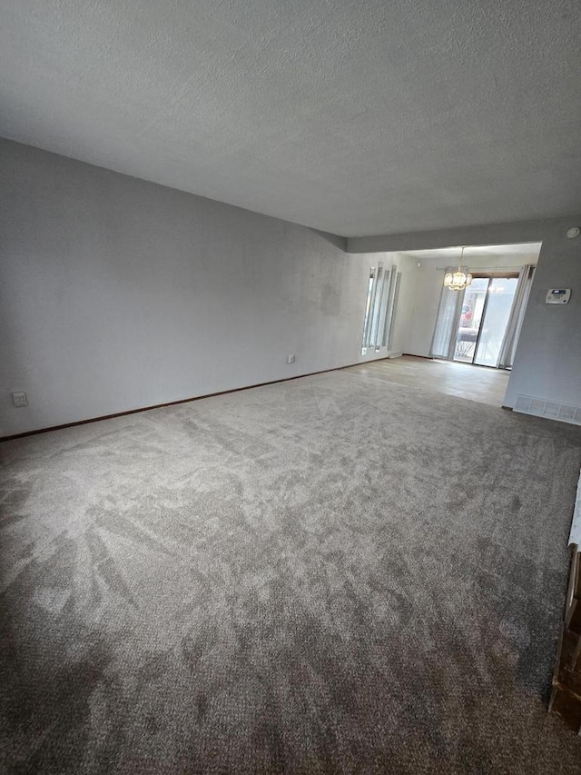 unfurnished room featuring carpet flooring, a textured ceiling, and a notable chandelier