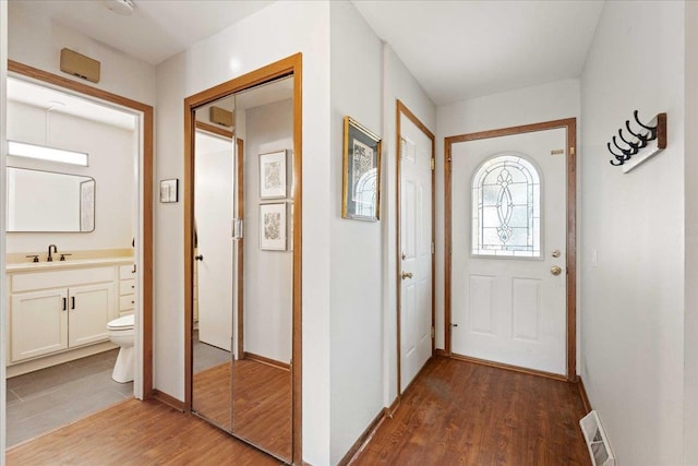 entryway with baseboards, wood finished floors, visible vents, and a sink