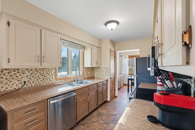 kitchen with stainless steel appliances, a sink, light countertops, stone finish flooring, and backsplash