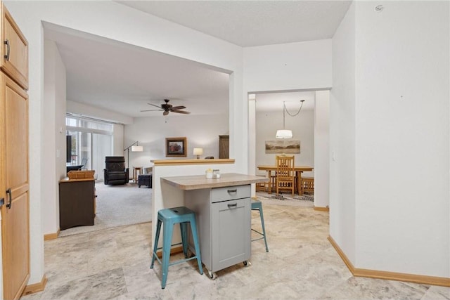 kitchen with a breakfast bar, ceiling fan, hanging light fixtures, a center island, and light carpet