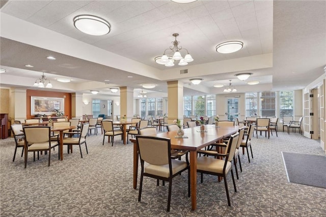 carpeted dining room featuring ornate columns, a chandelier, and a tray ceiling