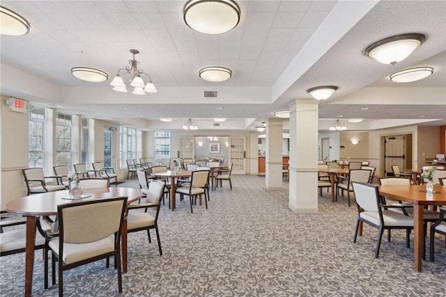 carpeted dining area featuring decorative columns, a chandelier, and a tray ceiling