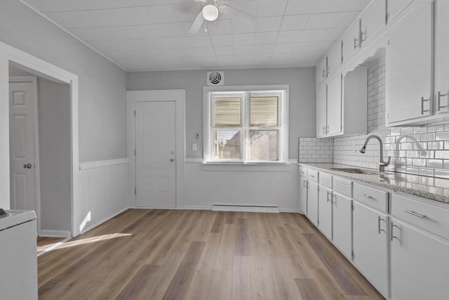 kitchen featuring white cabinetry, sink, a baseboard heating unit, light stone counters, and light hardwood / wood-style floors