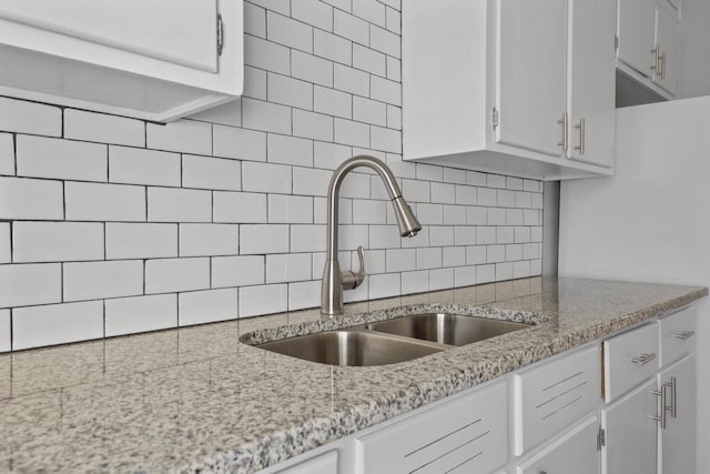 kitchen featuring sink, white cabinets, light stone counters, and decorative backsplash