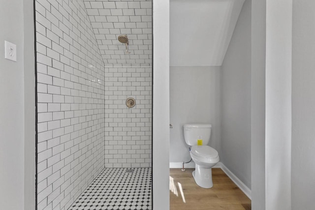 bathroom with a tile shower, hardwood / wood-style flooring, vaulted ceiling, and toilet