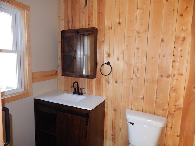 bathroom with vanity, wooden walls, and toilet