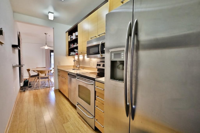 kitchen with pendant lighting, stainless steel appliances, sink, and light hardwood / wood-style floors