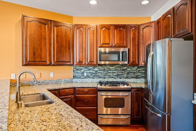 kitchen with tasteful backsplash, light stone countertops, appliances with stainless steel finishes, and sink