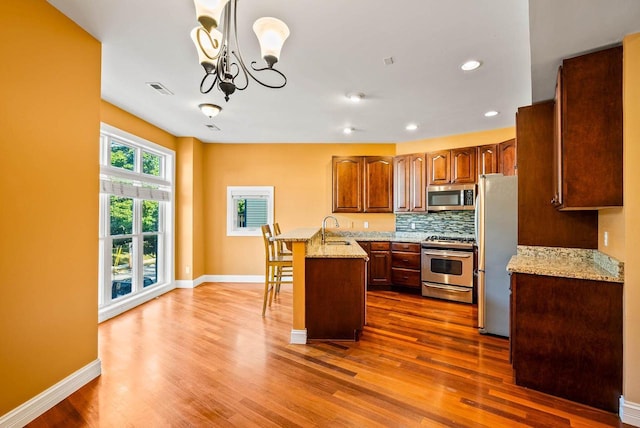 kitchen with a kitchen island, a breakfast bar, pendant lighting, stainless steel appliances, and light stone countertops