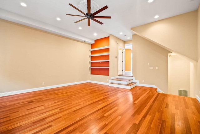 unfurnished living room with built in shelves, ceiling fan, and light hardwood / wood-style flooring