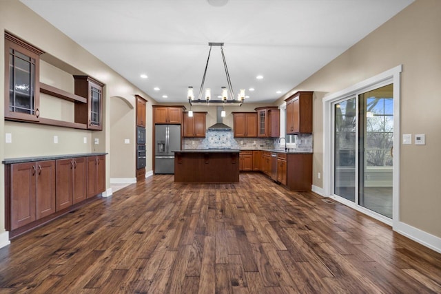 kitchen with pendant lighting, appliances with stainless steel finishes, dark hardwood / wood-style floors, a kitchen island, and wall chimney exhaust hood