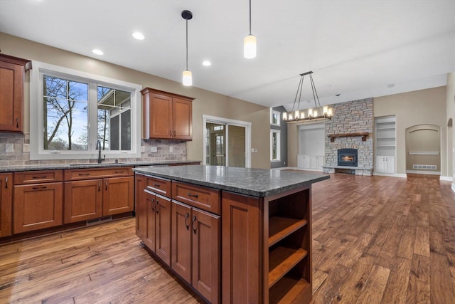 kitchen with decorative light fixtures, sink, dark stone countertops, a center island, and light wood-type flooring