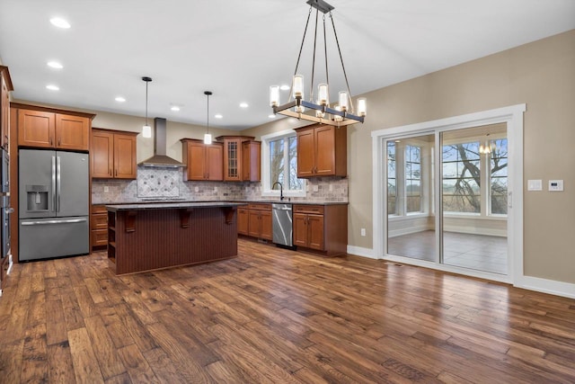 kitchen featuring wall chimney exhaust hood, a breakfast bar, a center island, hanging light fixtures, and appliances with stainless steel finishes