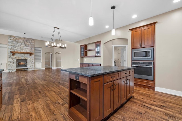 kitchen with decorative light fixtures, a center island, appliances with stainless steel finishes, dark hardwood / wood-style flooring, and dark stone counters