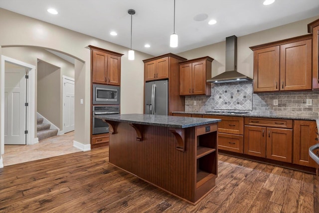 kitchen featuring wall chimney exhaust hood, a breakfast bar area, dark stone countertops, a kitchen island, and stainless steel appliances