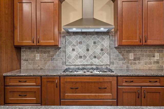 kitchen featuring dark stone countertops, stainless steel gas cooktop, wall chimney range hood, and decorative backsplash