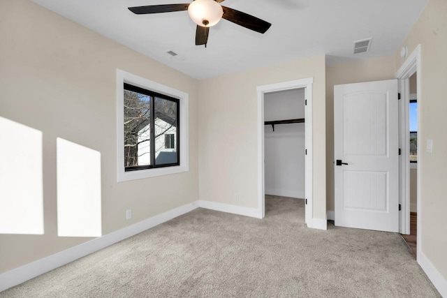 unfurnished bedroom featuring ceiling fan, light colored carpet, a closet, and a walk in closet