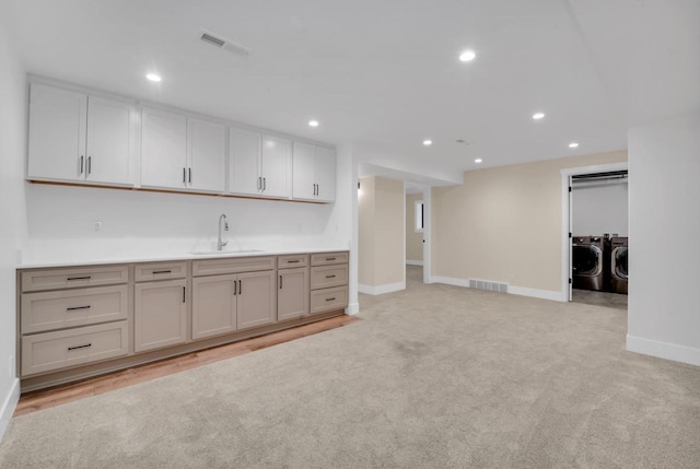 kitchen featuring light colored carpet, washer and clothes dryer, and sink