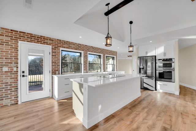 kitchen featuring brick wall, a kitchen island, decorative light fixtures, white cabinets, and stainless steel appliances