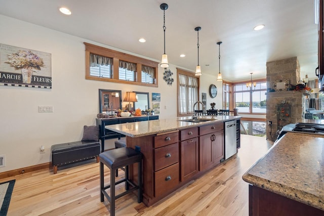 kitchen with pendant lighting, sink, light hardwood / wood-style flooring, a kitchen island with sink, and stainless steel dishwasher